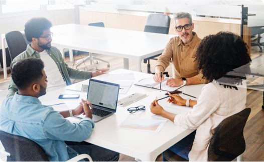 Group of 4 people sitting at table looking at laptops