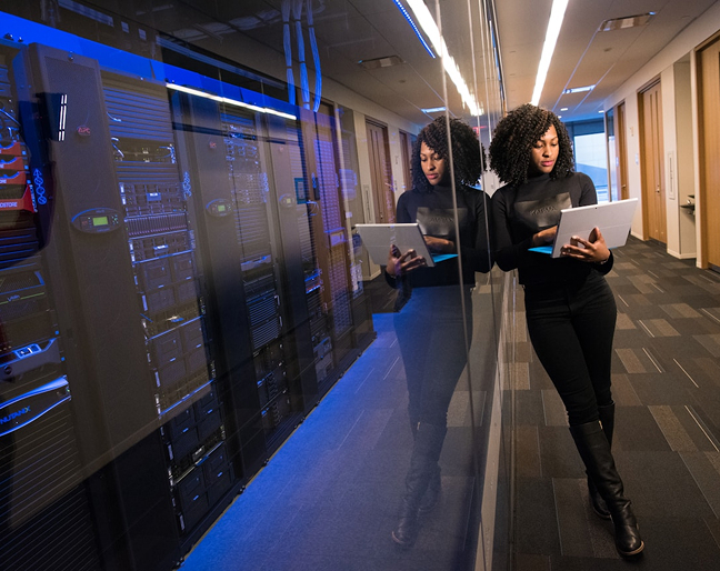 African American woman standing leading on wall while holding laptop